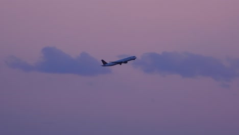 Large-airplane-takes-off-into-purple-red-sunset-haze-sky-rising-from-airport