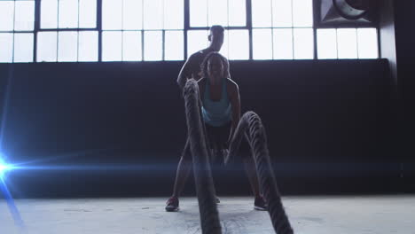 Blue-spot-of-light-against-african-american-woman-training-with-battle-rope