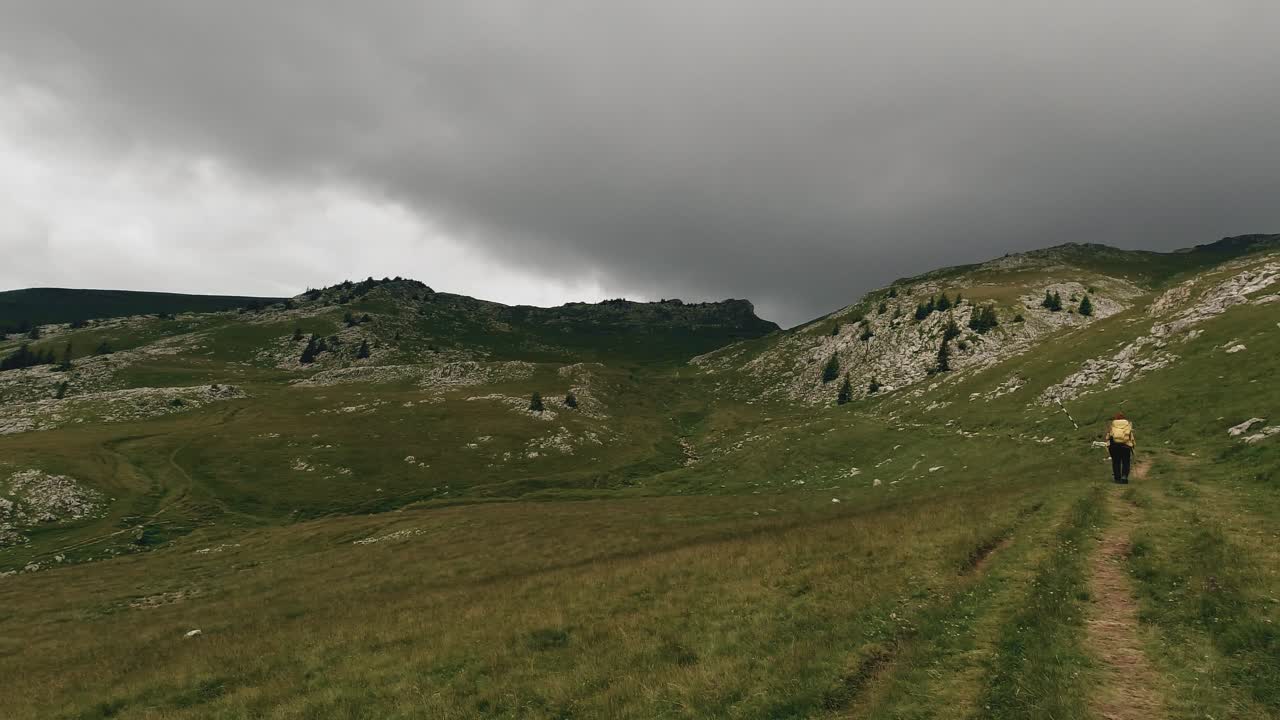 toma de gran angular que revela a un excursionista cruzando un valle alpino de montaña y algunas nubes de tormenta
