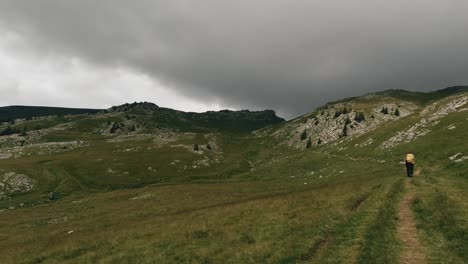 一幅廣角拍攝,顯示一個徒步旅行者穿過山高山山谷和一些暴風雲