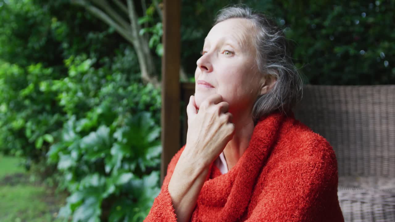 Happy senior caucasian woman sitting in garden, looking around and thinking