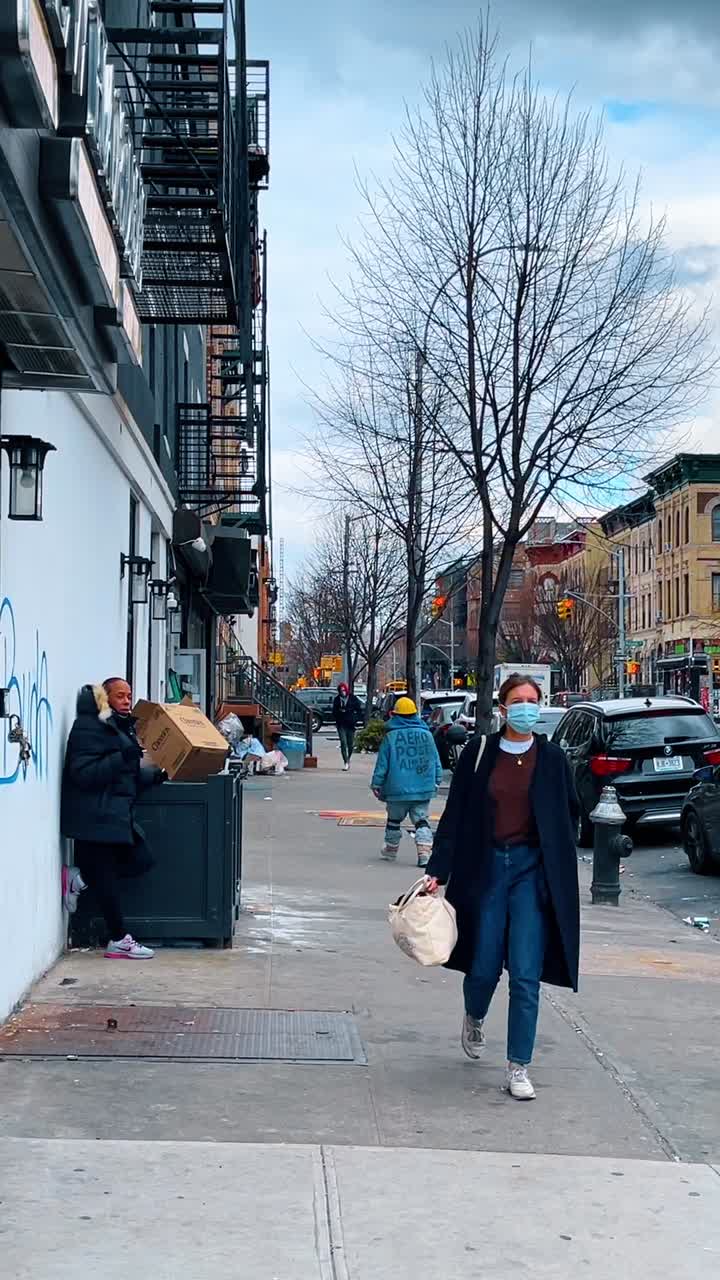 Nowy Jork, USA, 25 września 2025: Ludzie idący po miejskim chodniku w pobliżu ceglanych budynków. Szeroki widok pieszych na miejskiej ulicy z drabinami ewakuacyjnymi, nagimi drzewami i zaparkowanymi samochodami pod pochmurnym niebem.