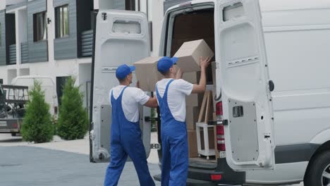 two young workers of removal company are loading boxes and furniture into a minibus