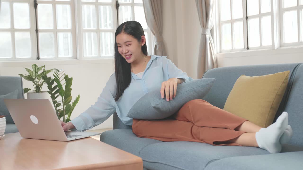 Asian Female Use Laptop Computer In Living Room While Lying On Sofa, Video In 4K
