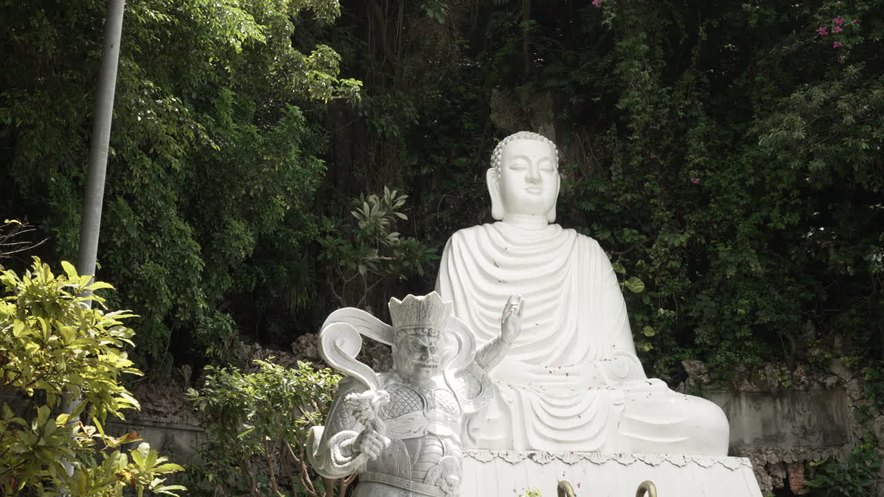 A white Buddha statue and guardian figure in a peaceful garden setting in Vietnam