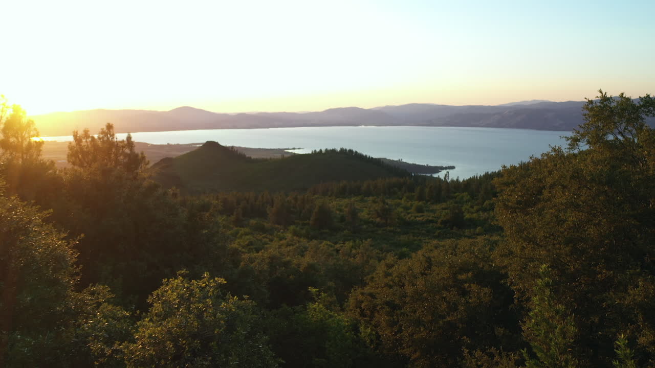 Flygfoto med drönare av solreflex genom träden på Mount Konocti vid solnedgången, som visar Clear Lake i Kelseyville, Kalifornien