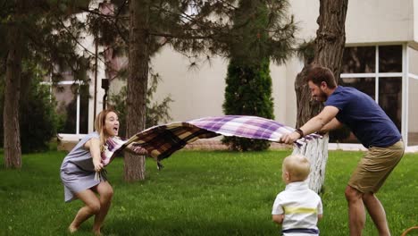 slow motion of a young family with a son on a green lawn. parents are spreading the plaid. excitement. blonde little boy on a forward perspective