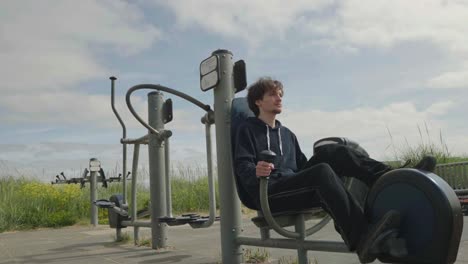 Young-man-working-out-on-exercise-bike-at-outside-gymnasium,-locked-off