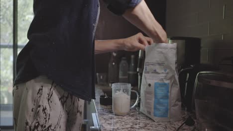 man scooping powdered milk into a blender cup in the kitchen