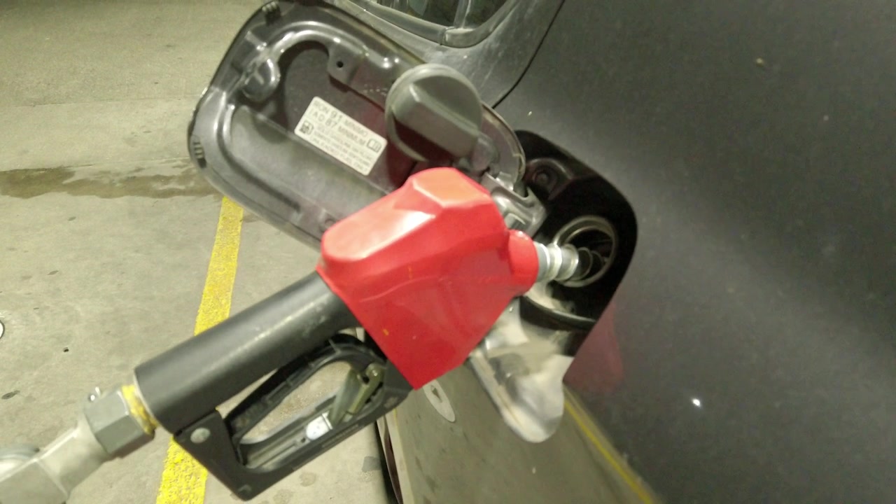 Primo piano di una pistola erogatrice di carburante che pompa benzina nel serbatoio di un'auto in una stazione di servizio, con consumo energetico dei trasporti e processo di rifornimento durante la notte
