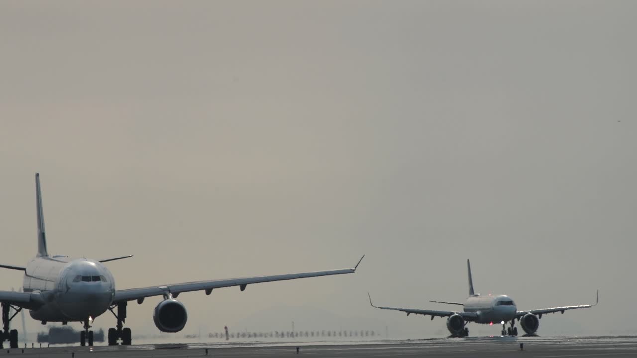 Two Cathay Pacific airplanes next to each other on the runway taxiing to arrive at the terminal