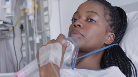 African-american-female-patient-with-oxygen-mask-lying-in-bed-in-hospital-room,-slow-motion