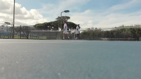 diverse male tennis players holding rackets and shaking hands at court