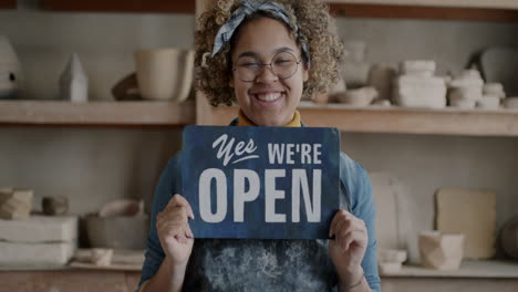 woman owner of pottery studio holding open sign