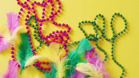 video de rosas y verdes perlas de carnaval de mardi gras y plumas sobre fondo amarillo con espacio de copia