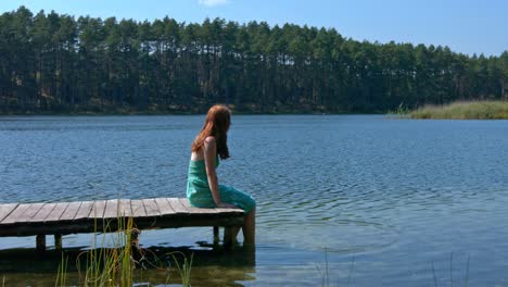 mujer pelirroja solitaria mirando hacia el lago mientras se sienta en el muelle