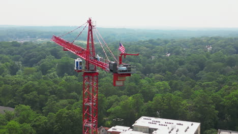 detailed view of tall red tower crane with large american flag waving in wind high above ground