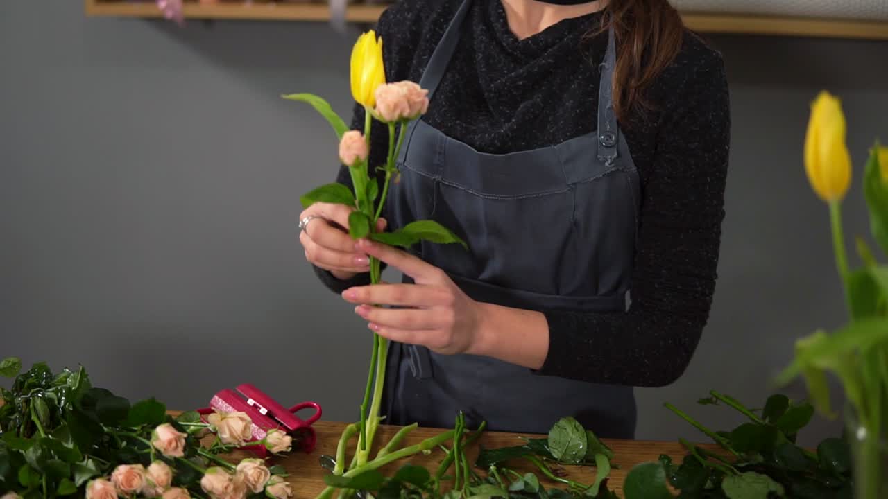 Young female florist arranging modern bouquet at flowers shot. She combines creamy roses and yellow tulips. Slow Motion shot