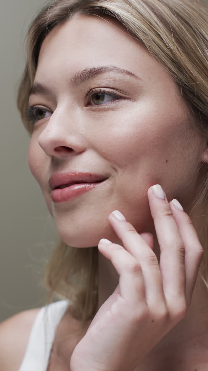 Vertical video of smiling caucasian woman with blond hair touching face, copy space, slow motion