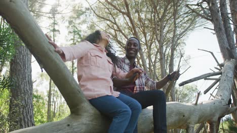 Sonriente-Pareja-Diversa-Tomados-De-La-Mano-Y-Sentados-En-Un-árbol-En-El-Campo