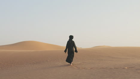 follow me shot of a beautiful muslim woman with hijab walking barefoot in a windy desert 2