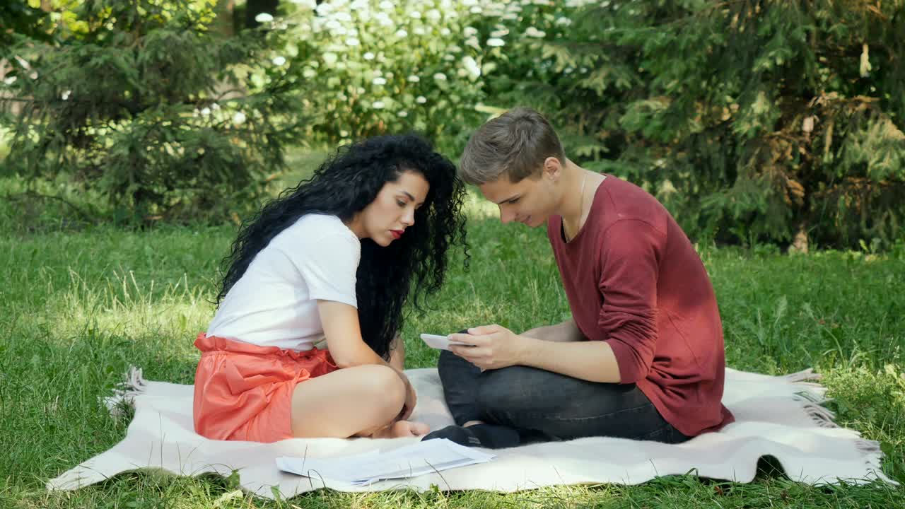 귀여운 커플이 플레이드 공원에서 스마트폰을 사용합니다.