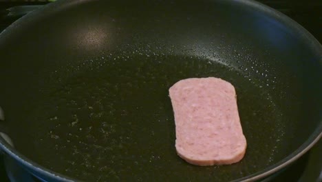 placing 2 pieces of spam into a frying pan to cook a cholesterol breakfast close up