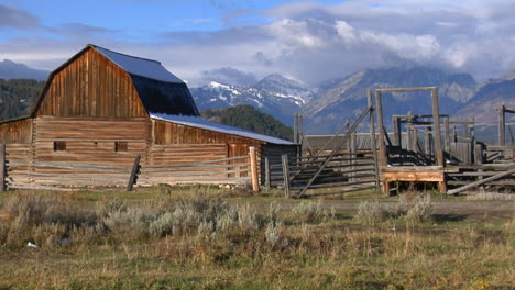 un viejo granero surge de una pradera con los grand tetons al fondo 2