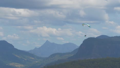 Parapente-Sobre-Un-Bosque-Verde-Con-Una-Cordillera-De-Fondo-En-Un-Día-Soleado---Interior-De-La-Costa-Dorada,-Australia