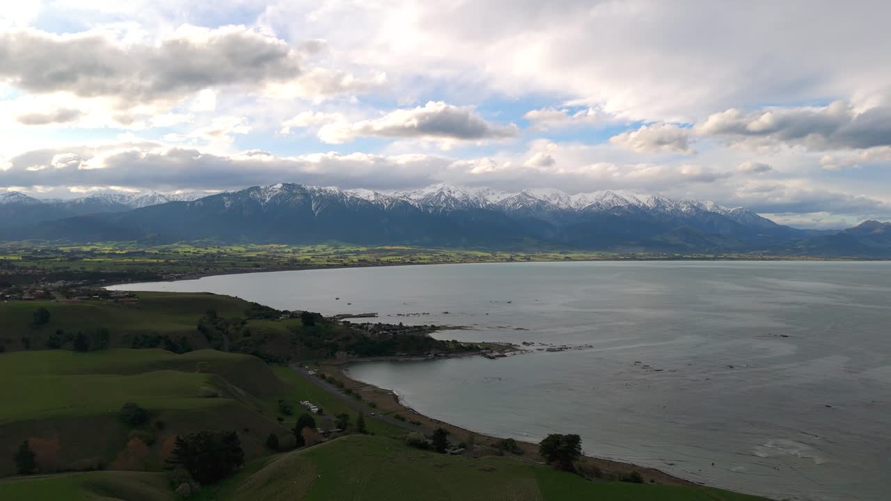 Forward drone flight reveals the coastal town of Kaikoura framed by the snow-covered peaks of the Southern Alps blending oceanfront scenery with dramatic alpine backdrops on New Zealand’s South Island