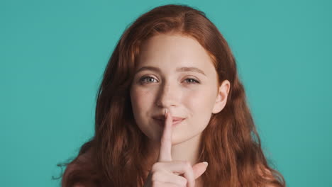 Redheaded-girl-talking-at-camera-on-turquoise-background.