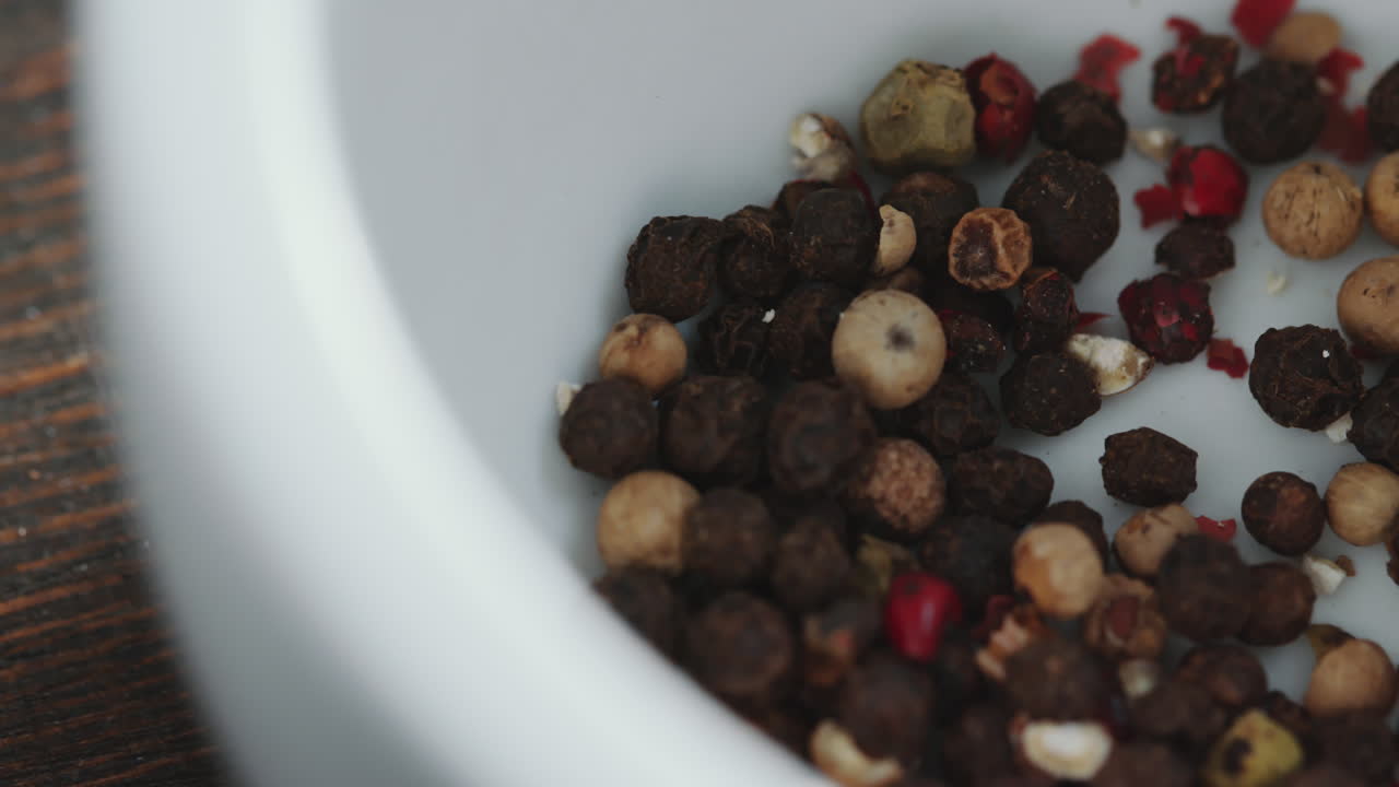 granos de pimienta y cristales de sal que caen en el mortero