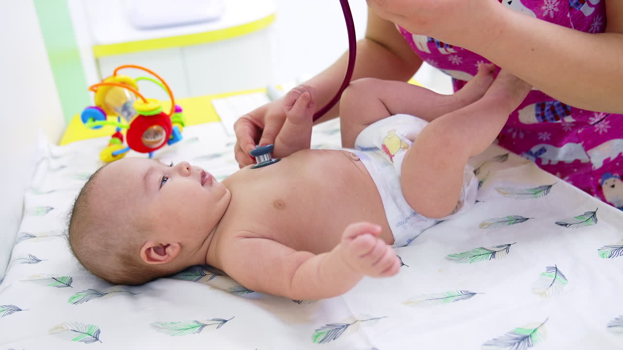 Pediatrician putting stethoscope to little boy's chest. Doctor distracting baby's attention by showing a colorful toy. Close up.