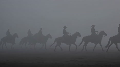 cowboys on horses in a foggy field