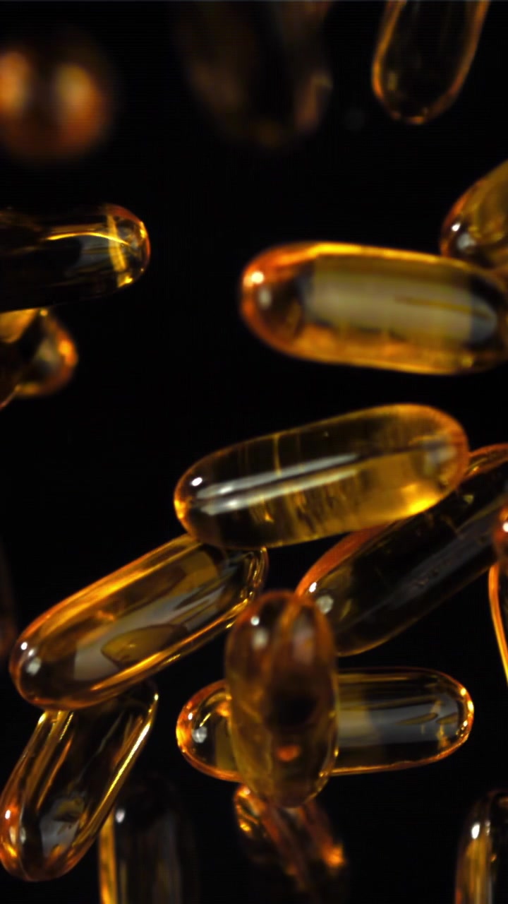 Capsule softgel dorate che si mettono a fuoco su sfondo nero.