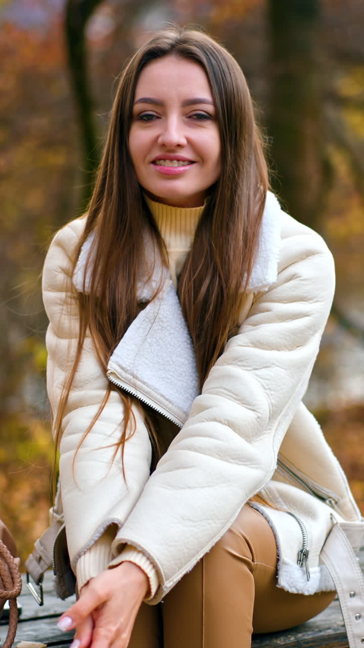Happy peaceful young woman enjoying autmn day in the nature. Brunette sits on the table in the park resting. Vertical video