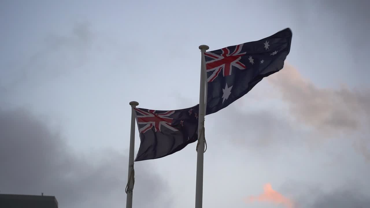 toma en cámara lenta que captura la bandera de australia y nueva zelanda ondeando lado a lado contra el cielo, aliados naturales con un fuerte sentido de familia trans-tasman