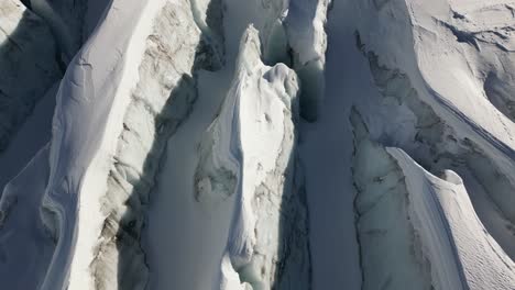 Aerial-top-view-of-glacier-crevasses-in-the-Swiss-alps,-snow-covered-peaks