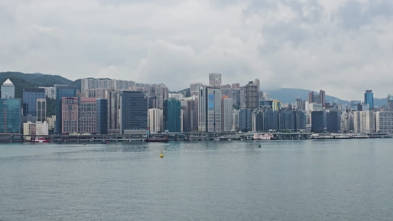 Slow pan sweeping Victoria Harbour's iconic Hong Kong Island skyline from Kowloon, revealing supertall towers like ICC, I Square, and The Cullinan against misty mountain backdrop