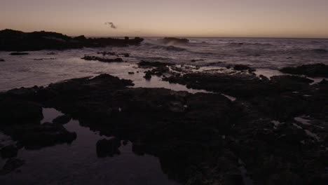 static shot of hawaii beachfront at dusk, as waves crash into rocks in the distant ocean