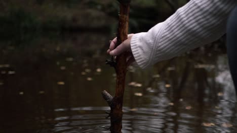 Hand-Entspannt-Sich-Mit-Stock-In-Der-Nähe-Von-Plätscherndem-Wasser,-Mittlere-Aufnahme