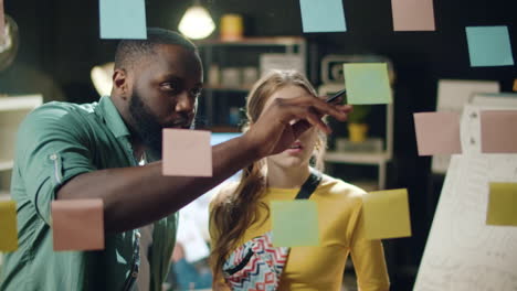 Annoyed mixed race couple working in office. Afro man pointing stickers