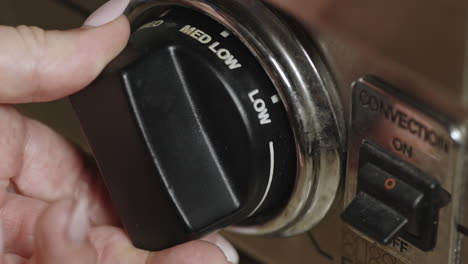 Woman&#039;s hand setting oven knob to medium low heat