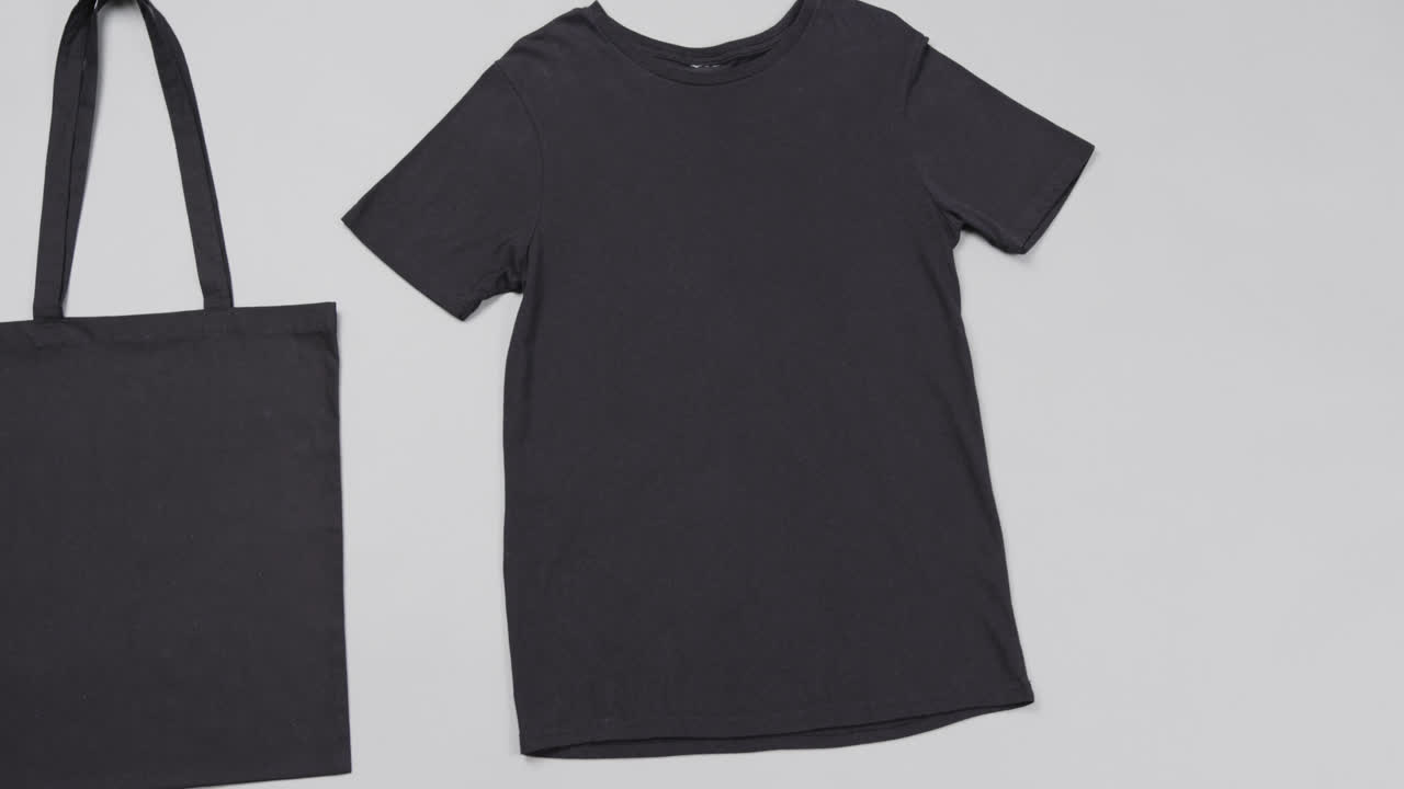 Primo piano di borsa nera e t-shirt su sfondo bianco, con spazio per il testo, al rallentatore