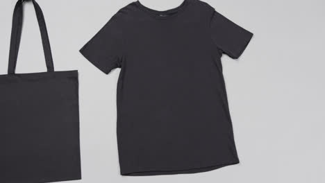 Close-up-of-black-bag-and-t-shirt-on-white-background,-with-copy-space,-slow-motion