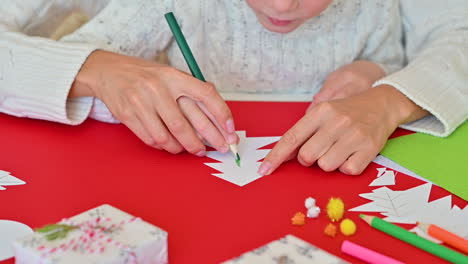 child colors a paper cutout christmas tree with a pencil. mother takes his hand to guide him and teach him how to do it. close-up.