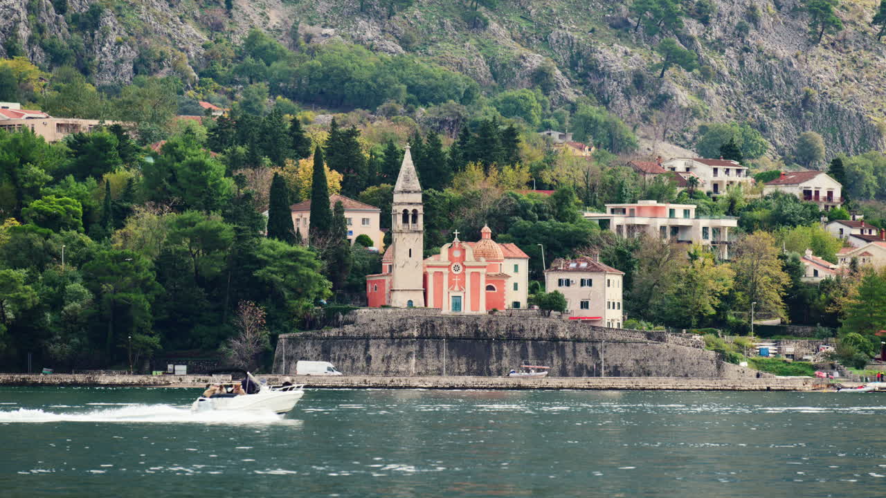 Chiesa di Sant'Eustachio situata su un muro fortificato sopraelevato lungo il lungomare della Baia di Cattaro con montagne.