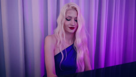 mujer rubia bonita en vestido tocando el piano en un pub o club nocturno iluminado con luces azules púrpuras - empujar en primer plano
