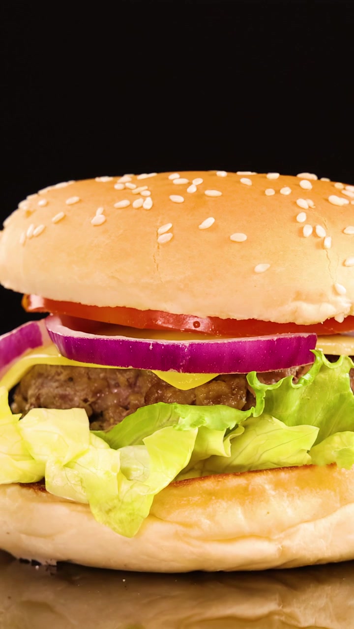 Succulento hamburger di manzo con lattuga, pomodoro, cipolla e formaggio ruota dolcemente sotto l'illuminazione da studio, evidenziando ingredienti freschi su uno sfondo nero pulito