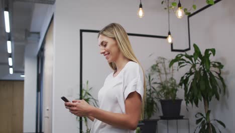 portrait of caucasian woman smiling while using smartphone at office